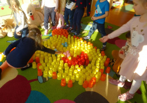Grupa dzieci wspólnie układa z kubeczków plastikowych głowę misia.